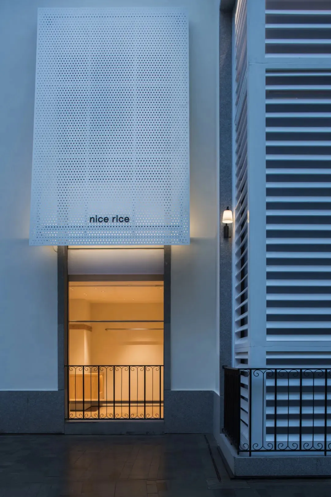 A calm and inviting building with a white exterior, black door, and a sign reading Nice Rice, photographed at night with contrasting lighting