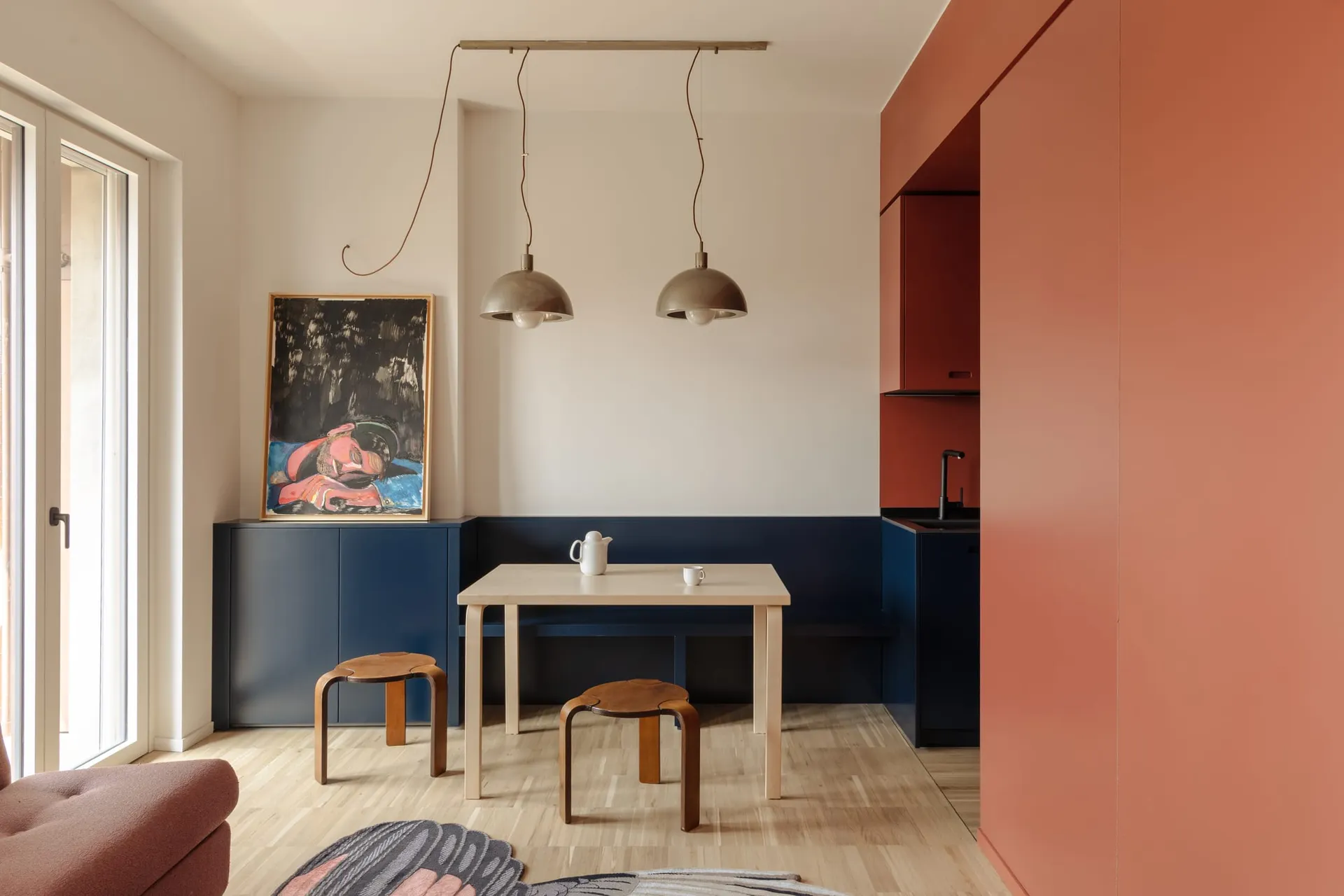 A well-lit living room with a wooden floor, a dining table, chairs, a couch, and a painting on the wall, creating a warm and cozy atmosphere