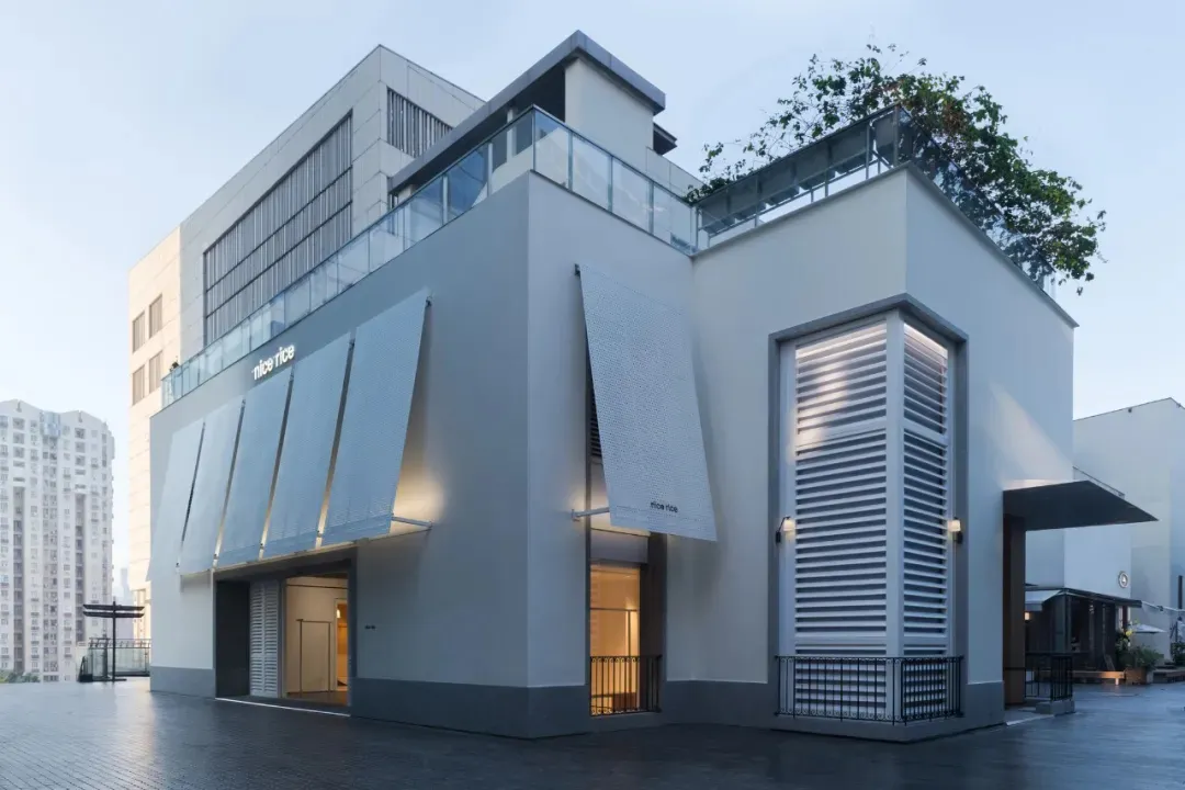 Photograph of a modern white building with large windows and smaller windows, made of concrete, in natural daylight