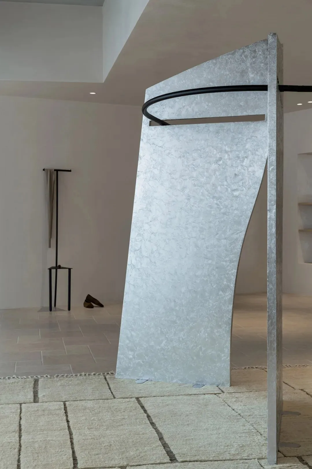 A bright and open gallery space with a large silver sculpture in the center, surrounded by a white color scheme