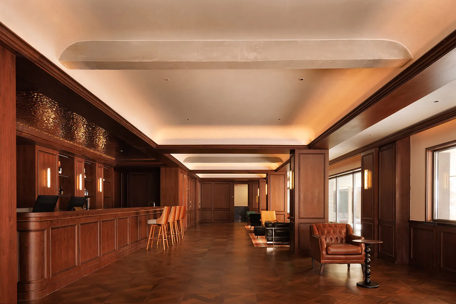 A modern lounge area with wooden floors and walls, featuring a bar, chairs, a couch, and a dining table, with a warm and inviting atmosphere