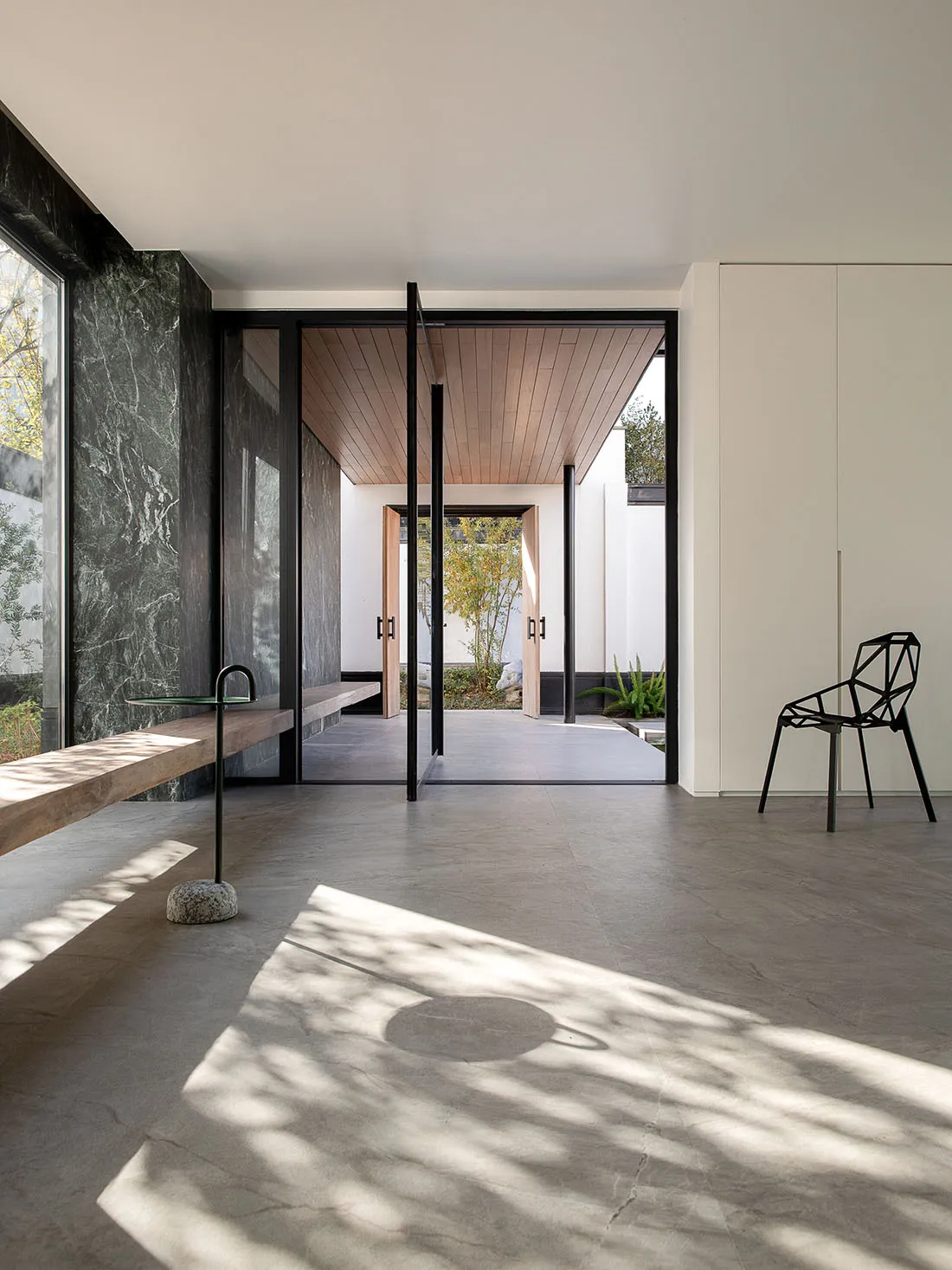 Bright and welcoming open living space with marble flooring, a black chair, a bench, and a dining table, filled with natural light