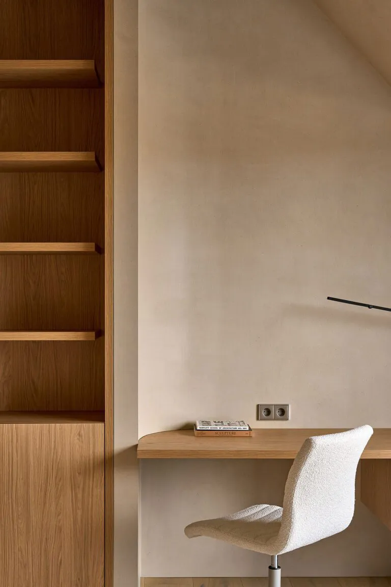 Cozy home office with a desk, chair, bookshelf, and couch in a room with white walls and a warm atmosphere