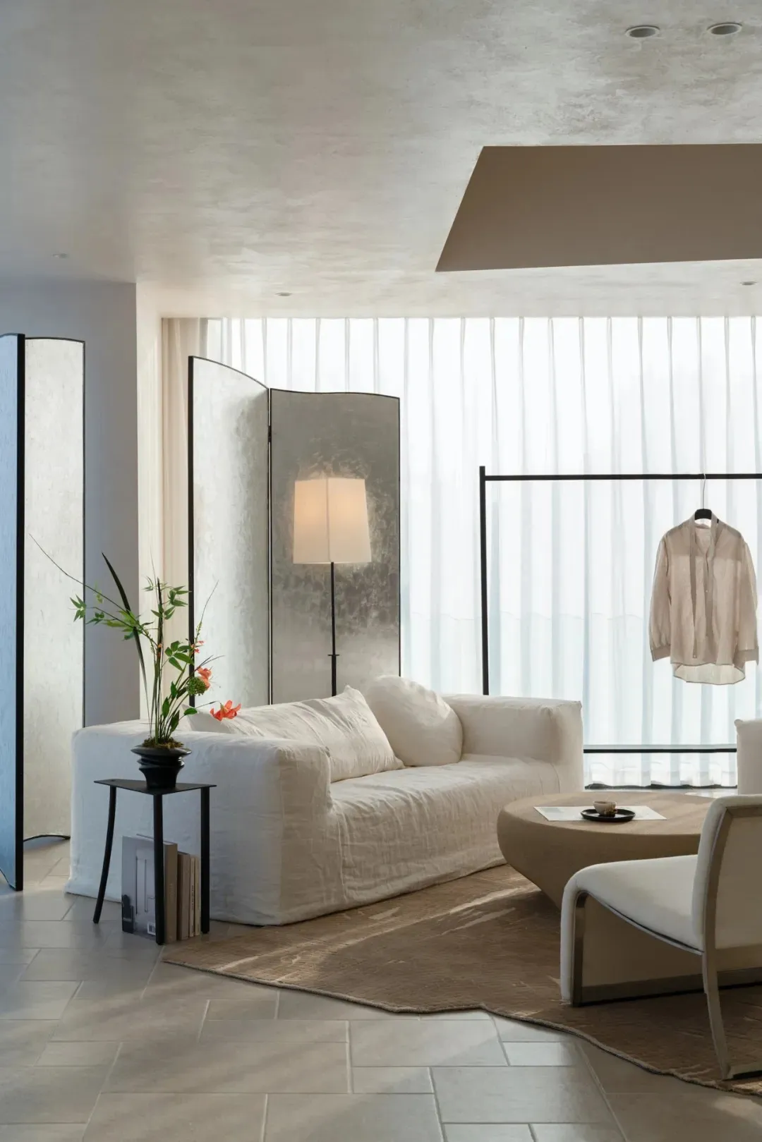 A modern living room with a white couch, chair, and potted plant, filled with natural light and a warm atmosphere