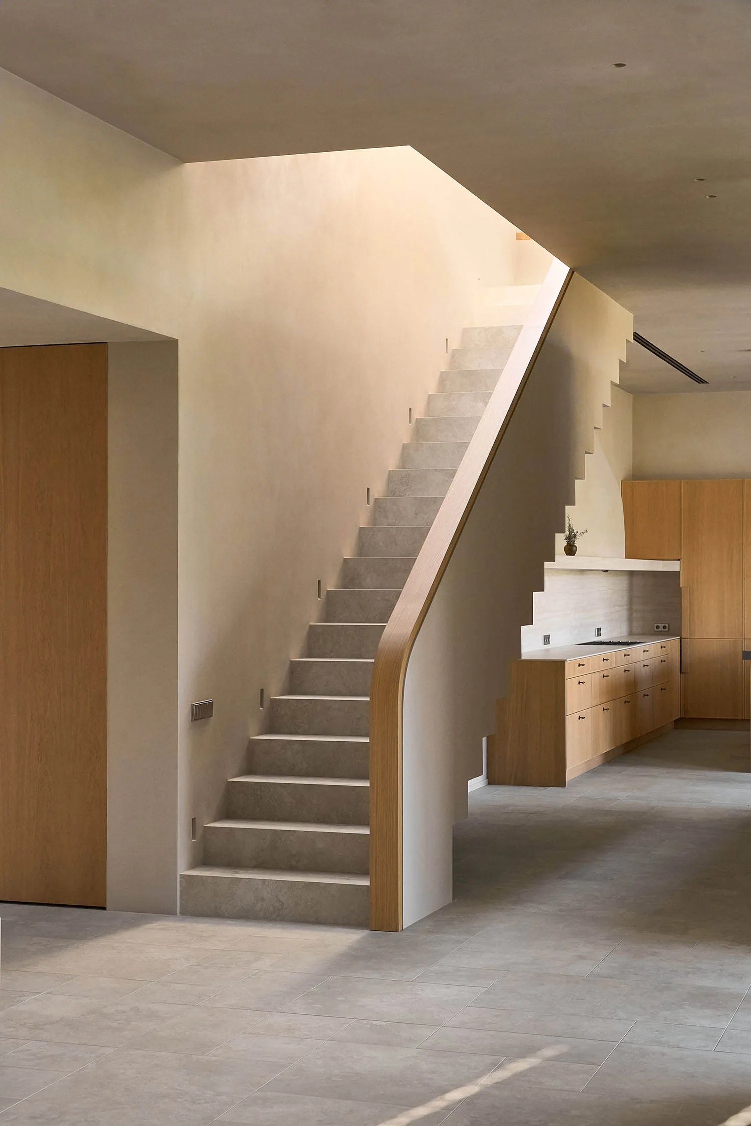 A dimly lit hallway with a wooden staircase, the walls and floor are not visible, the staircase is the main focus