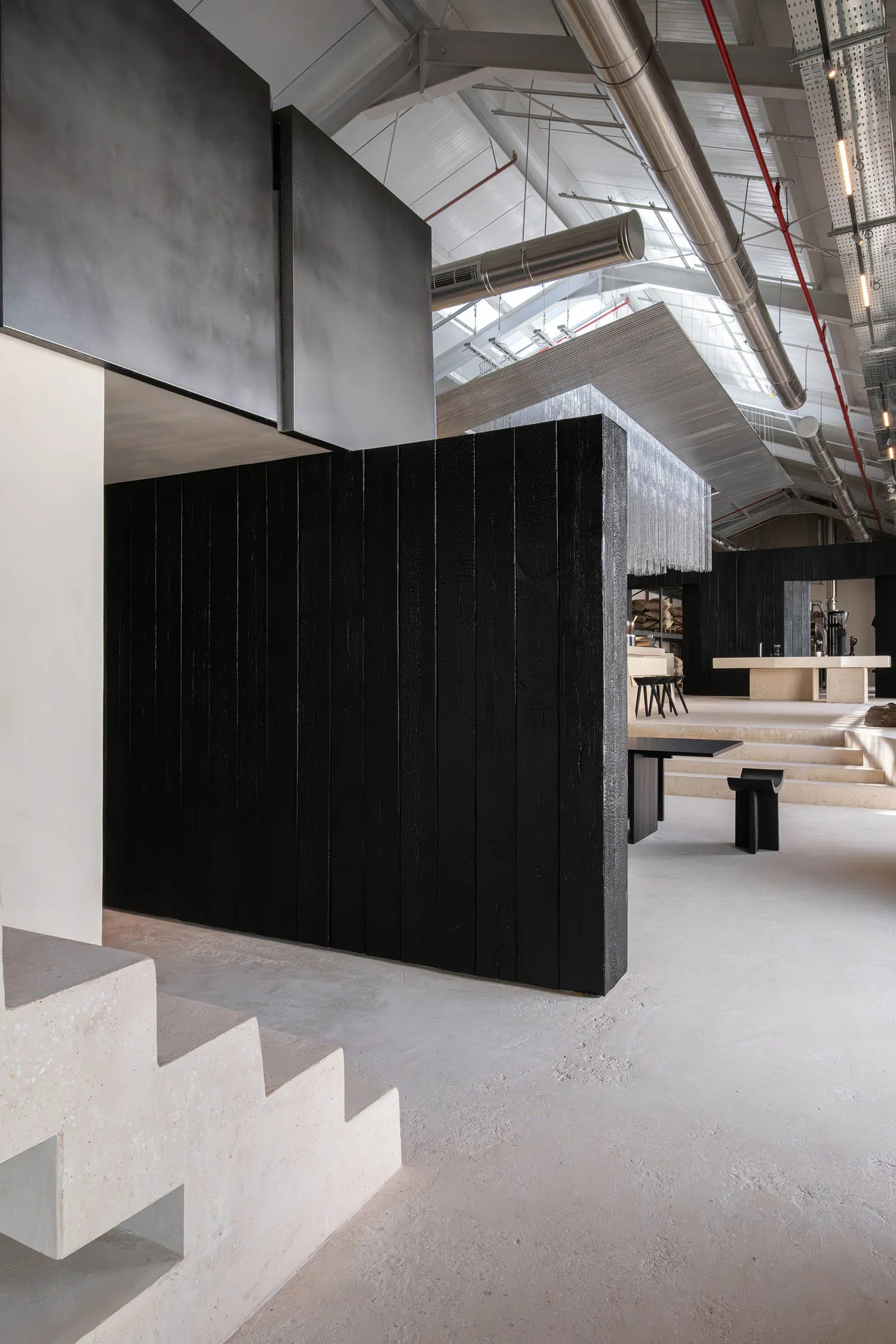 A large, open space with a black wall, a modern staircase made of concrete, and a minimalist design