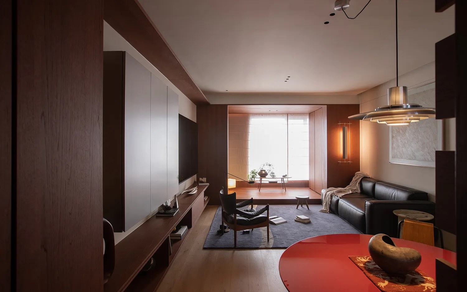 Cozy modern living room with a red table, a couch, a chair, and a TV, decorated with a vase, a bowl, and a book, with natural light and a warm atmosphere