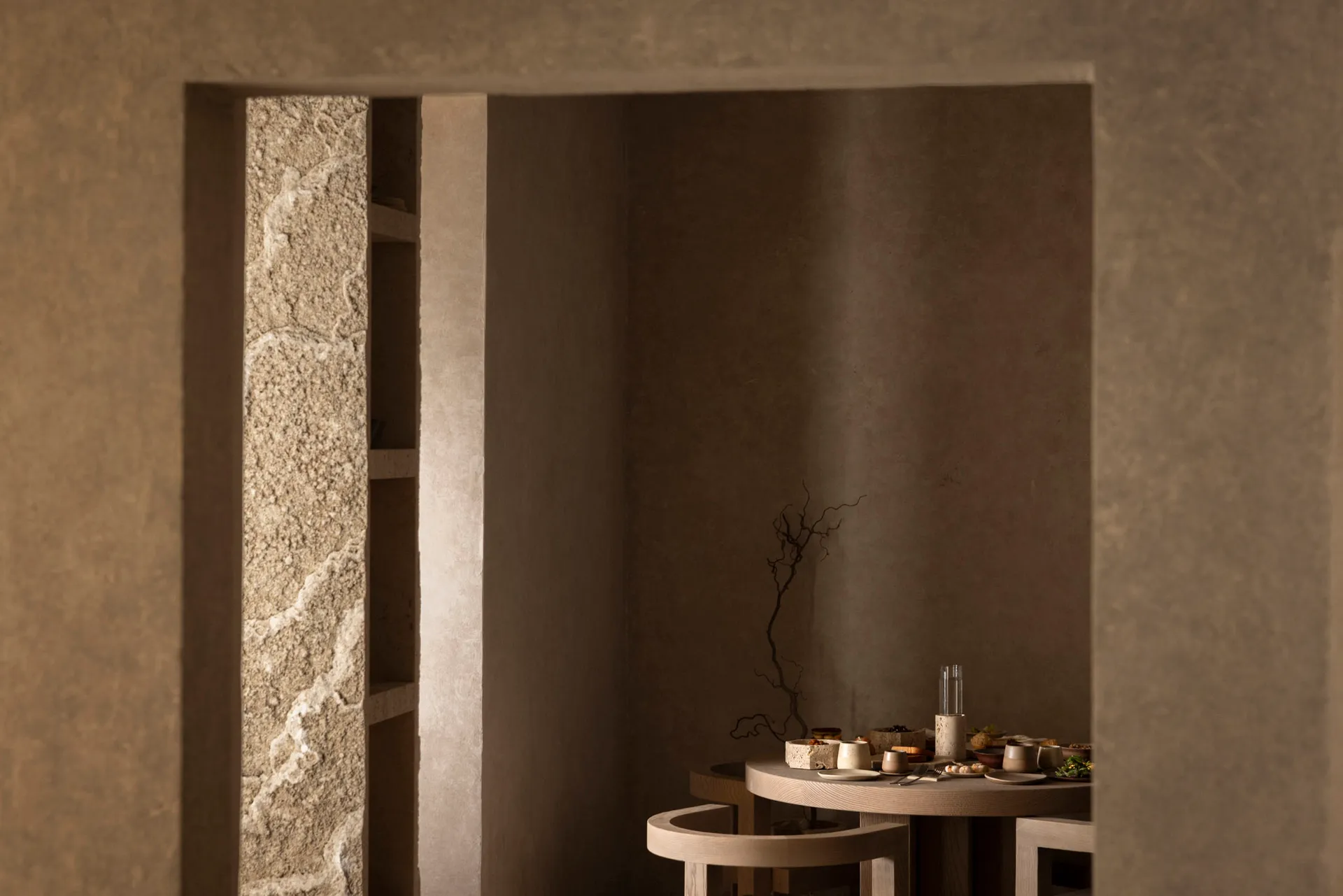 Cozy dining area with a stone table and chairs, surrounded by stone walls, with dim lighting and warm wood accents