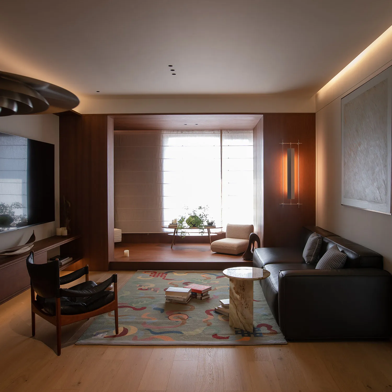 Cozy living room with a black couch, a chair, a dining table, and a potted plant, set against a wooden floor and surrounded by walls