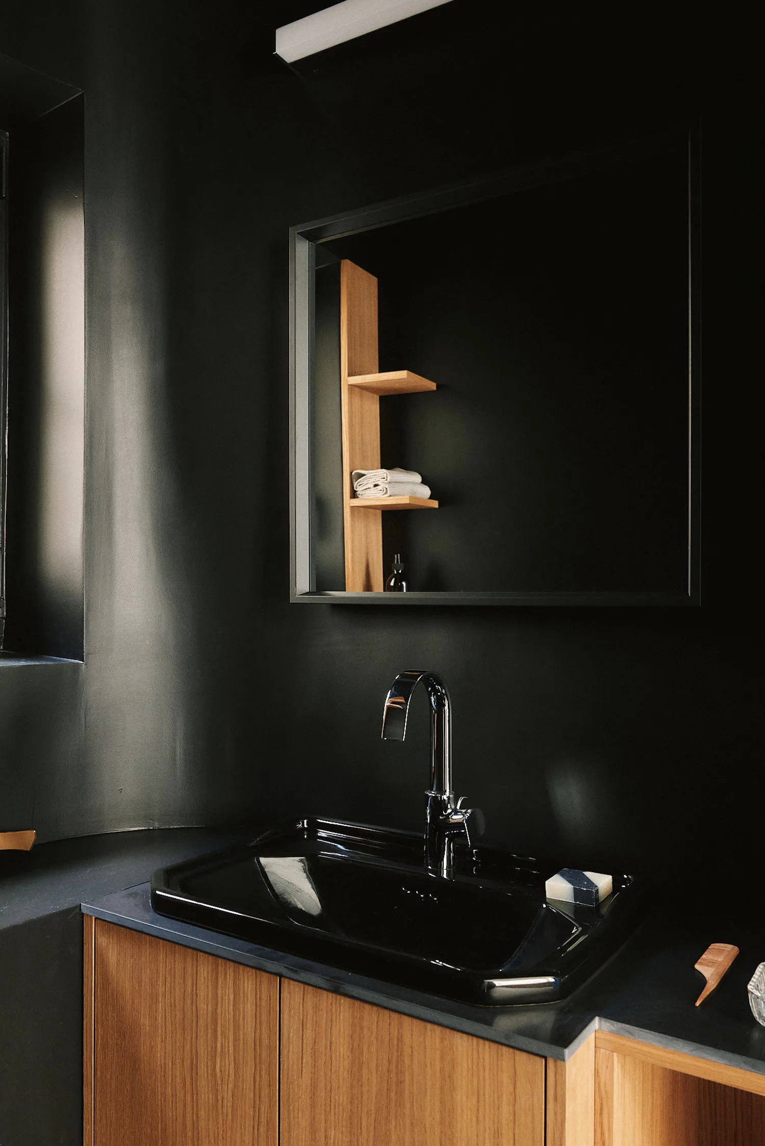 A black sink and mirror are the focus in a dark bathroom setting