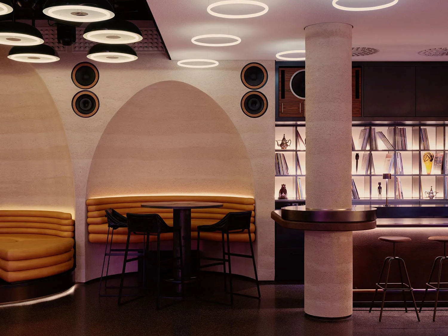 A well-lit restaurant interior with a bar, dining area, and modern decor, featuring a variety of books on the walls