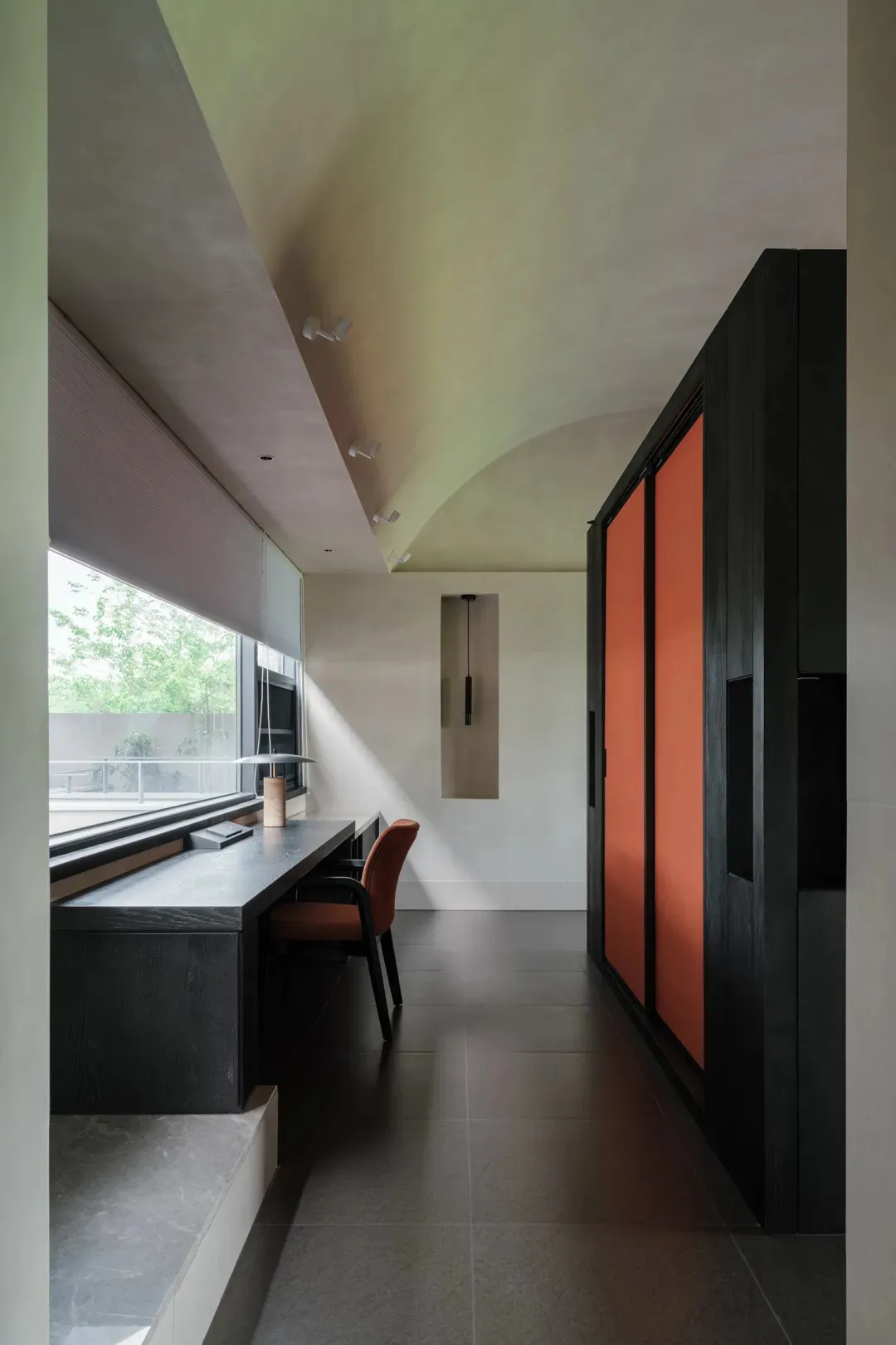 A modern living space with a black and orange color scheme, featuring a desk, chair, closet, and window