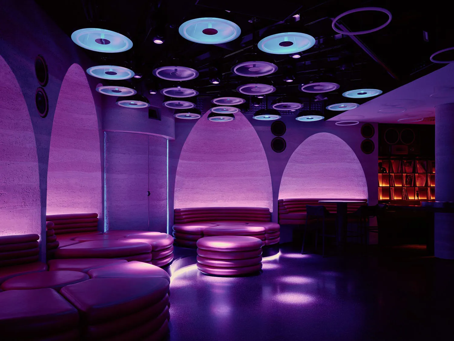 Purple-lit lounge with a futuristic design, featuring a circular shape and a dome-like ceiling, with couches and chairs throughout