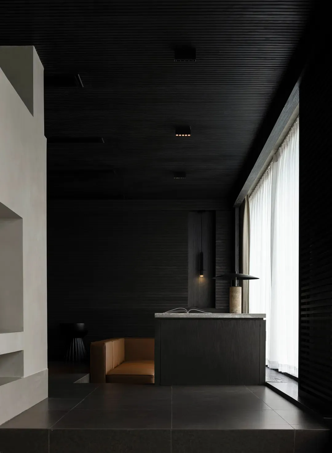 A dimly lit room with a wooden counter, a brown couch, and a window providing natural light, in a black and white color scheme