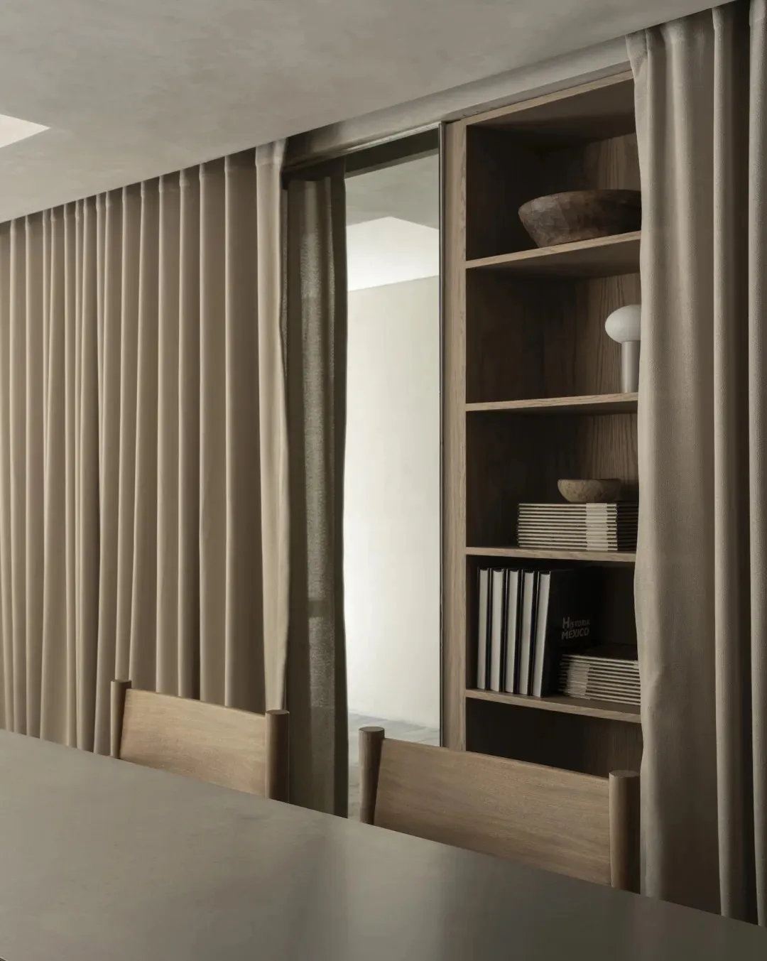 Dimly lit dining room with a wooden table and chairs, a brown curtain, and a bowl on the table