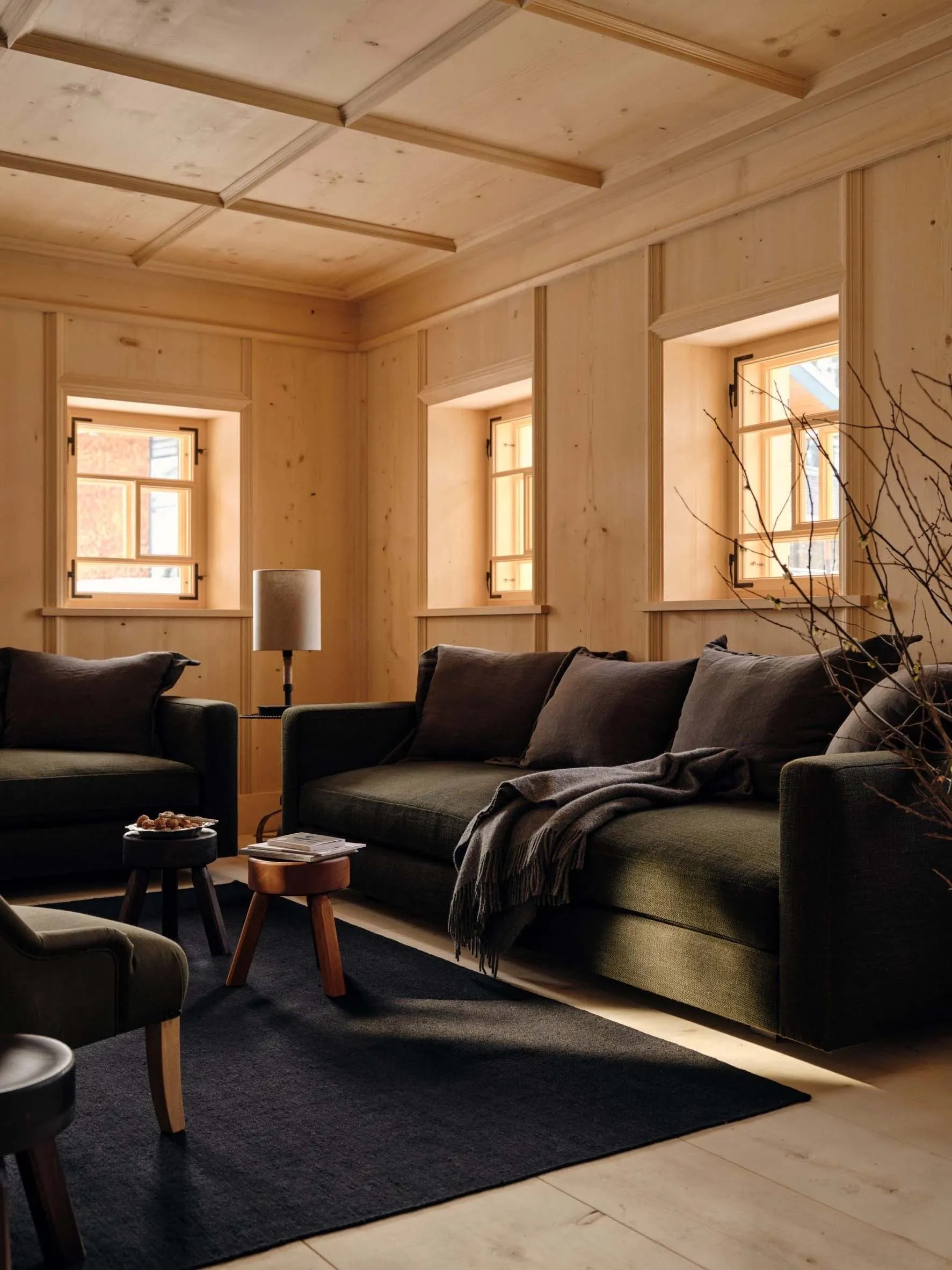Cozy living space with wooden walls and floors, a couch, chair, and coffee table, featuring soft and diffused lighting