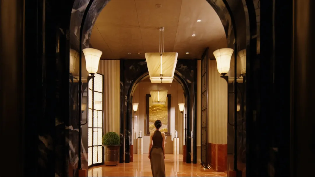 A woman walks through a grand hallway with marble flooring and a high ceiling, creating an elegant and sophisticated atmosphere