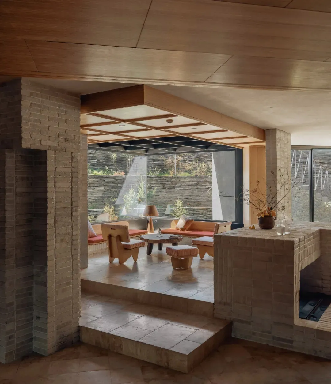 Warm and inviting living room with a stone fireplace, brick wall, stone floor, and stone countertop, furnished with a couch, chair, and dining table, with potted plants and vases adding to the ambiance