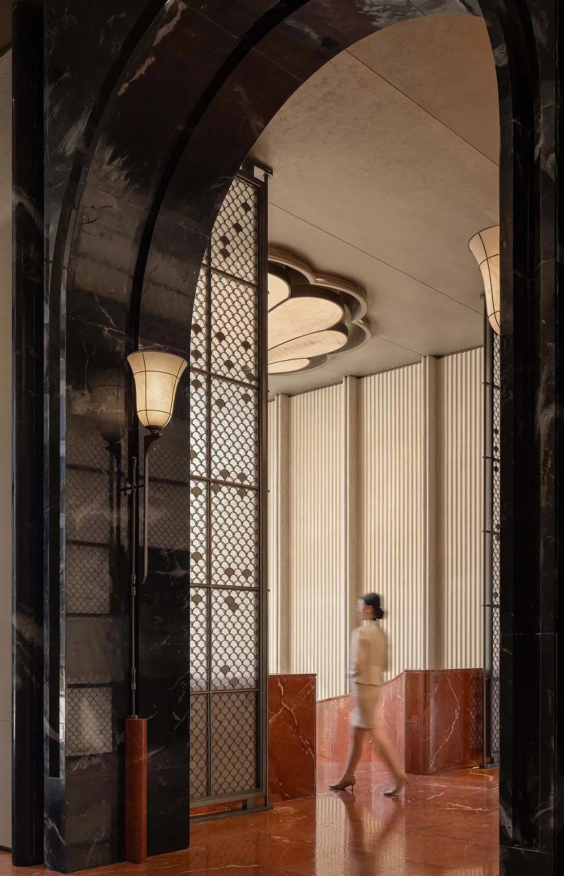 A woman walks down a hallway with marble flooring, surrounded by elegant decorations and dark tones