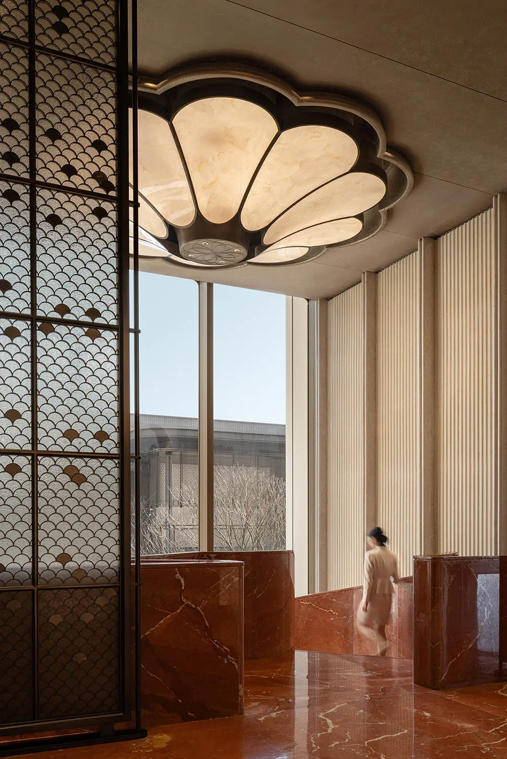 Well-lit lobby with a marble floor, marble wall, and marble ceiling, featuring a bench and a woman walking towards the camera