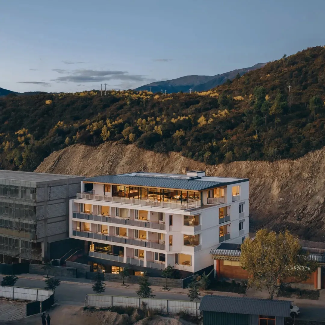 A modern hotel building with a concrete exterior, surrounded by trees and natural scenery, with soft and diffused lighting