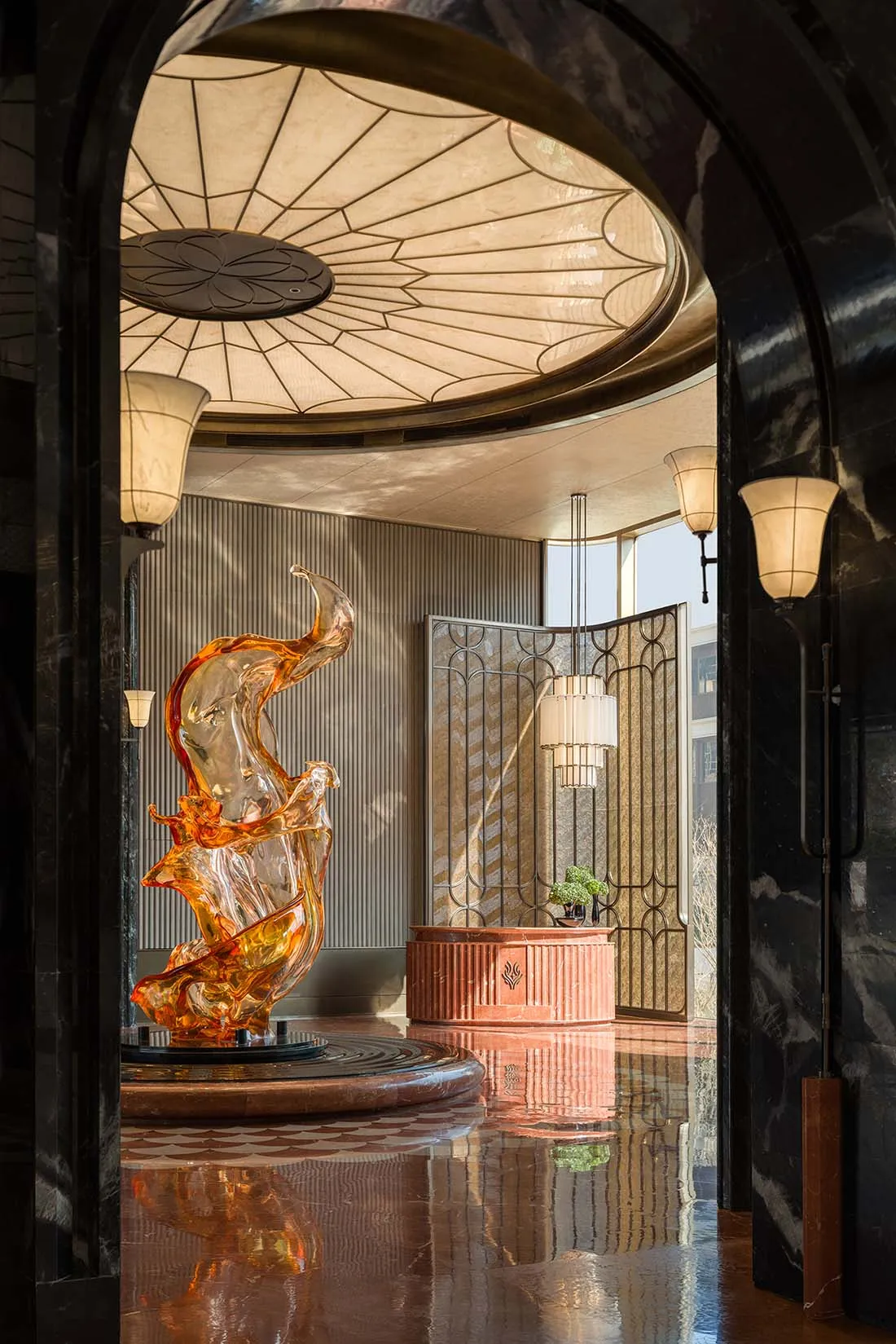 A modern lobby with a glass sculpture on a marble surface, surrounded by a pink and brown color scheme, and natural light from a large window