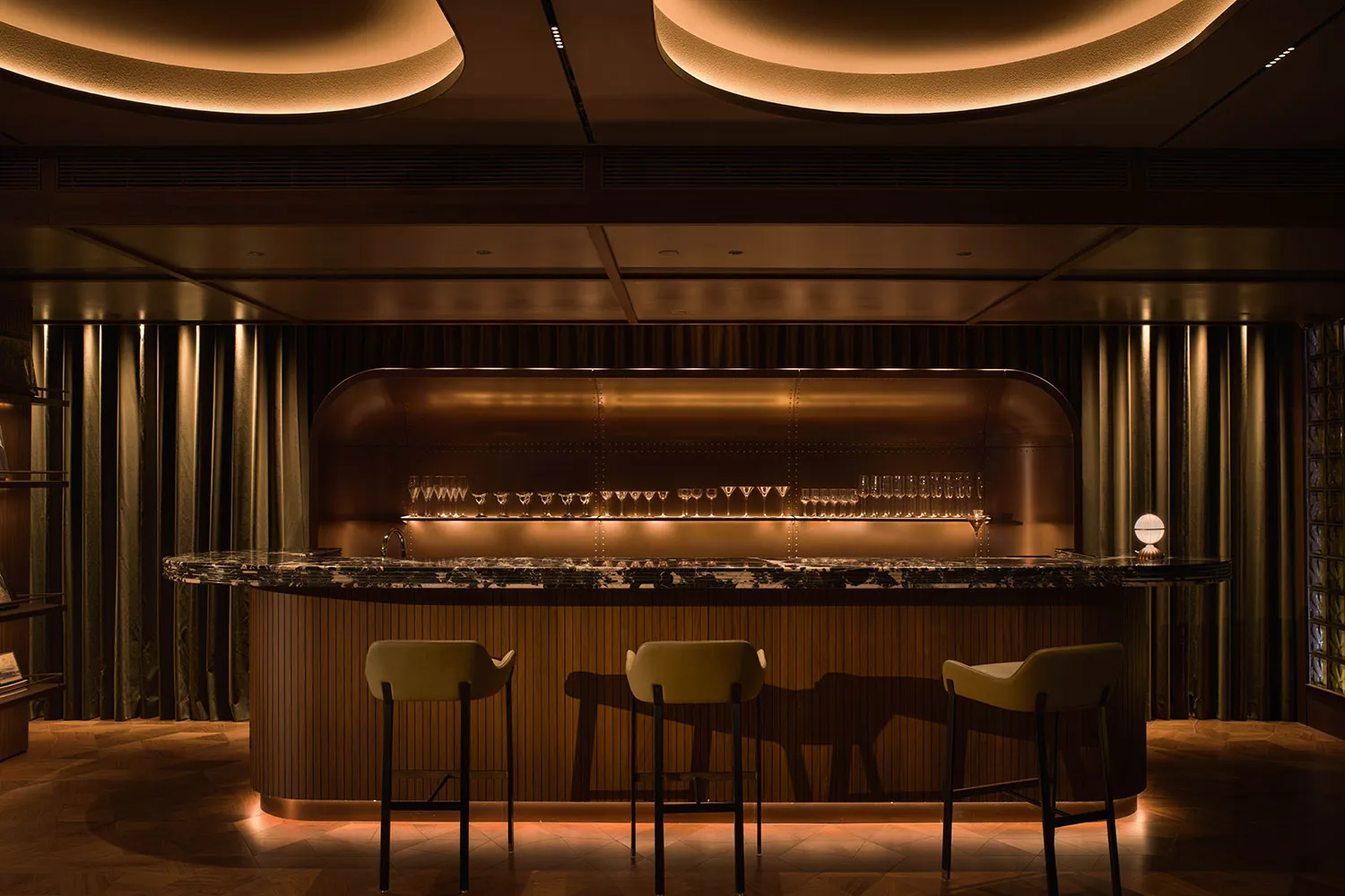 A cozy bar area with a wooden counter, chairs, and tables, featuring a brown color scheme and wine glasses