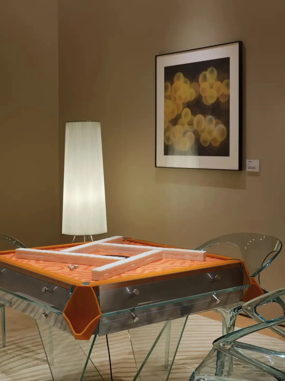 A well-lit living room with a glass dining table, two chairs, a couch, and a lamp, featuring glass and wood materials