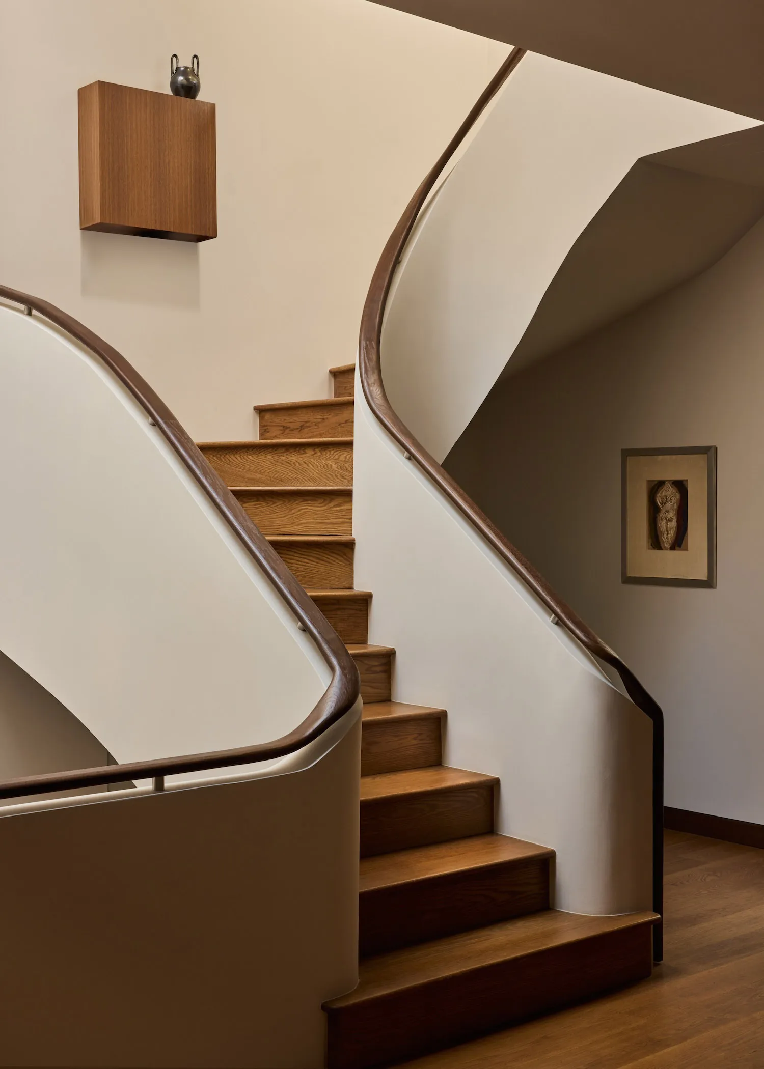 A modern staircase with a wooden railing in a residential hallway, bathed in natural light