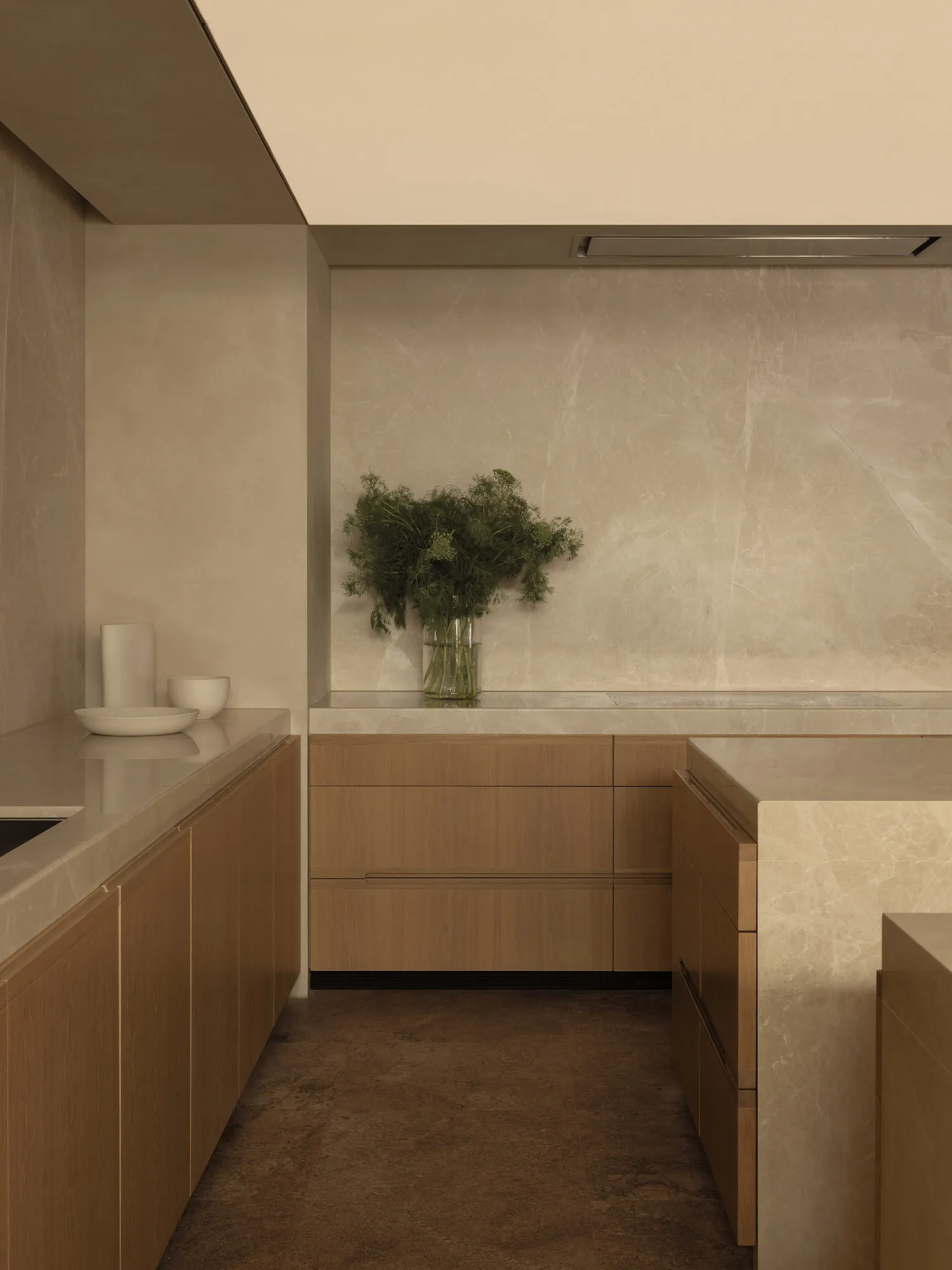 A modern kitchen with a white marble countertop, brown wooden cabinets, and natural light from a window