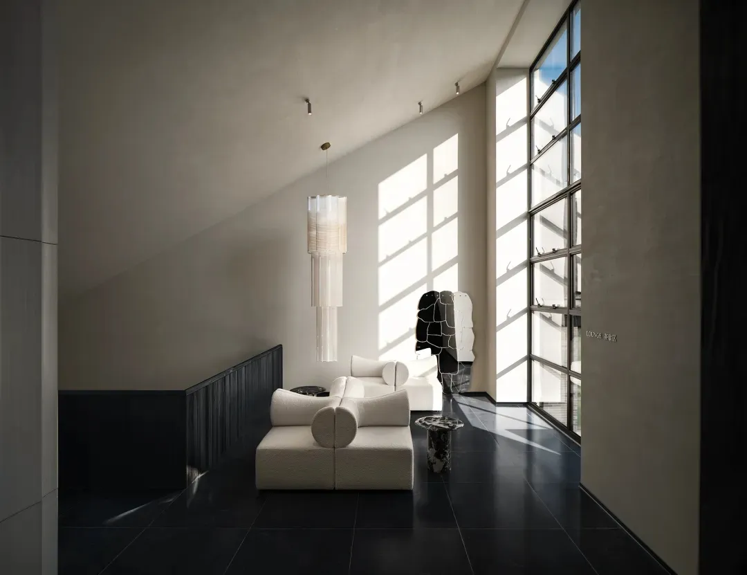 Dimly lit living room with a white couch and chair, large window, and modern simplicity