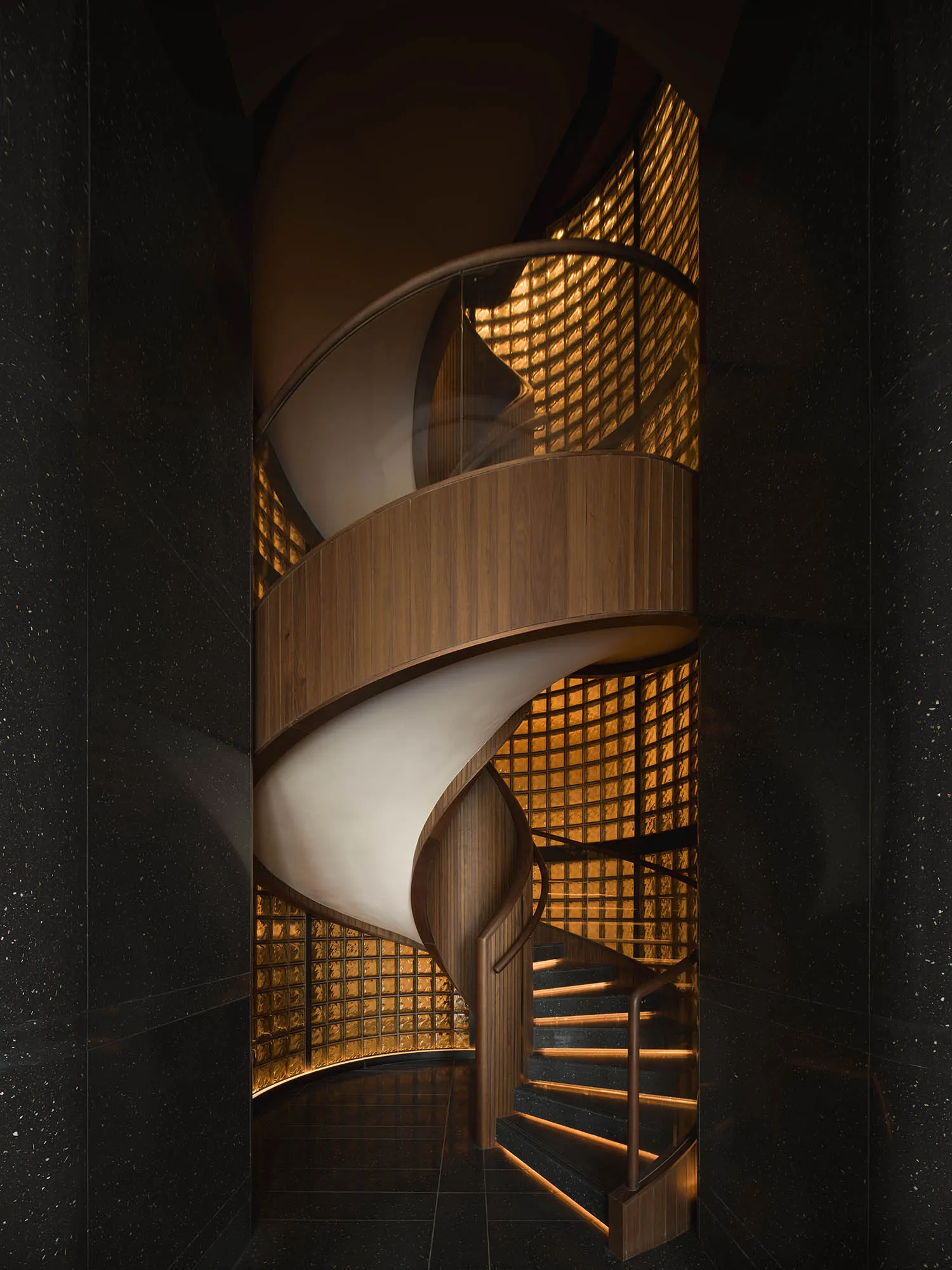 A spiral staircase in a dark room with a wooden staircase and metal railing