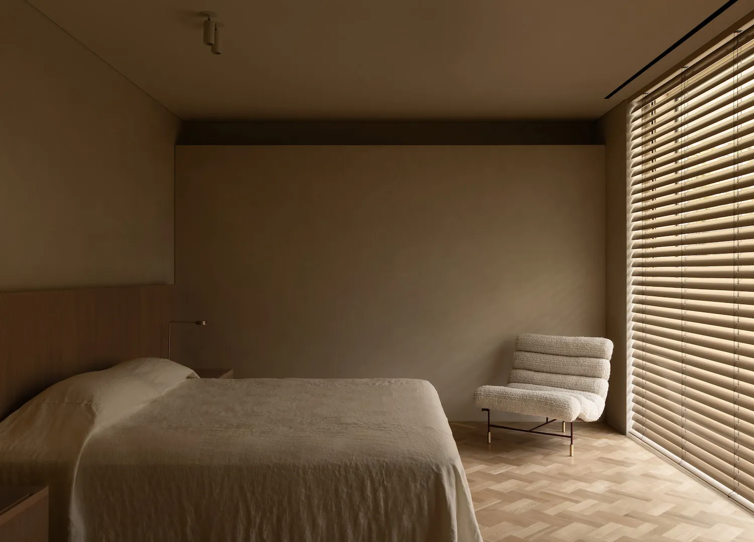A calm and inviting bedroom with a bed, chair, and window, featuring a mix of modern and traditional styles, neutral colors, and wooden elements, with natural light streaming in through the window