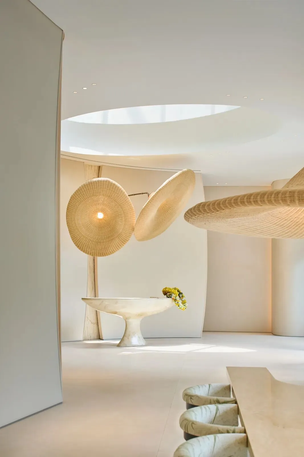 Modern minimalist room with a white floor, a metal bowl on a pedestal, a glass vase, and a light fixture providing illumination