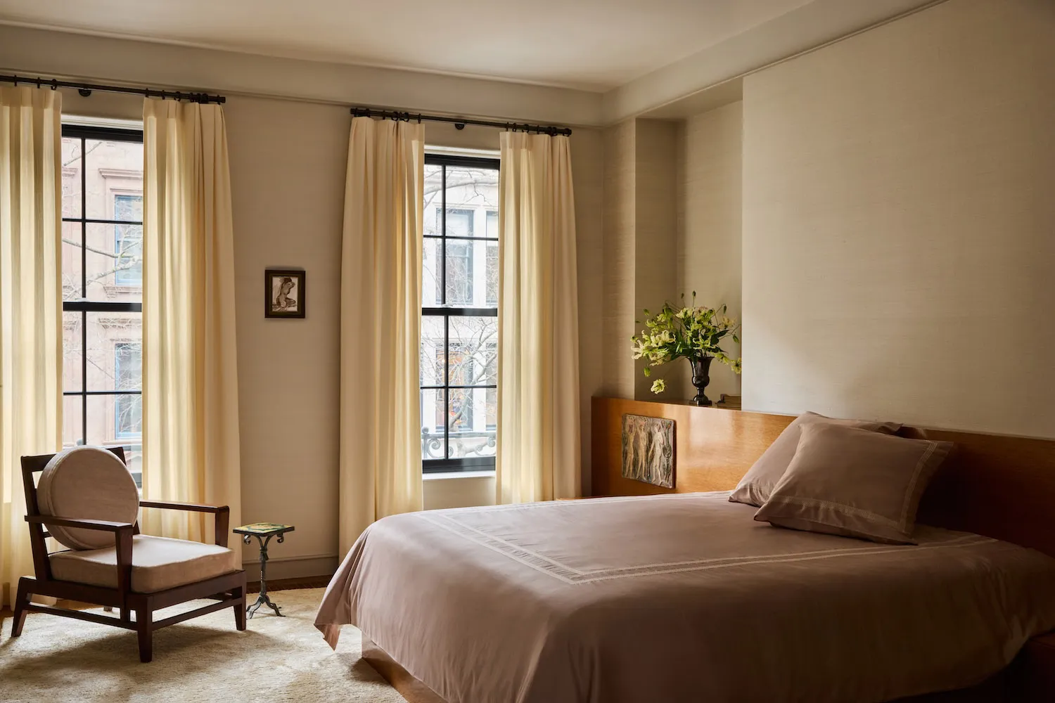 Cozy bedroom with a bed, chair, and window, featuring a pink blanket, flowers, and natural light