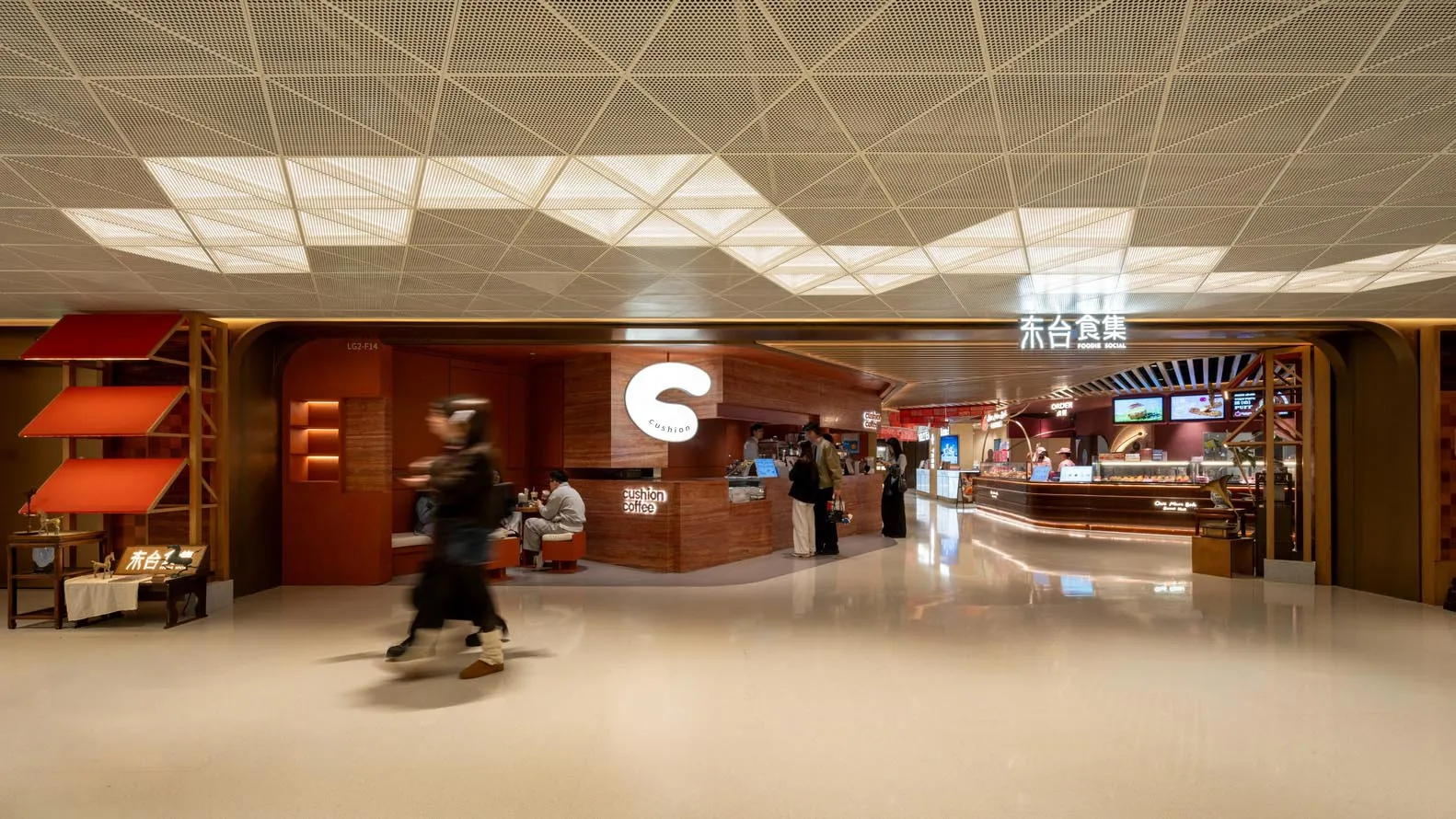 A large, open public space with a shiny floor, modern furniture, and natural light, filled with people walking, sitting, or standing