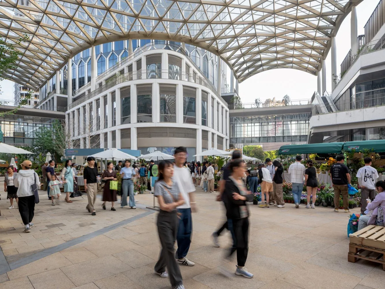 繁忙的城市街道上,人們朝不同方向行走,周圍是現代與傳統建築交錯的景象,人行道上擺放著雨傘