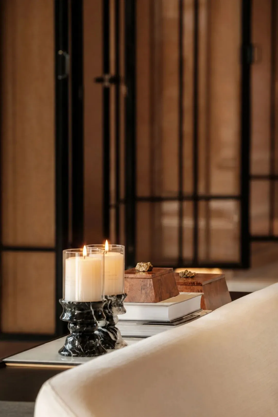 Cozy room with a wooden couch, a book, and a black table with two lit candles in glass vases, set against a neutral background