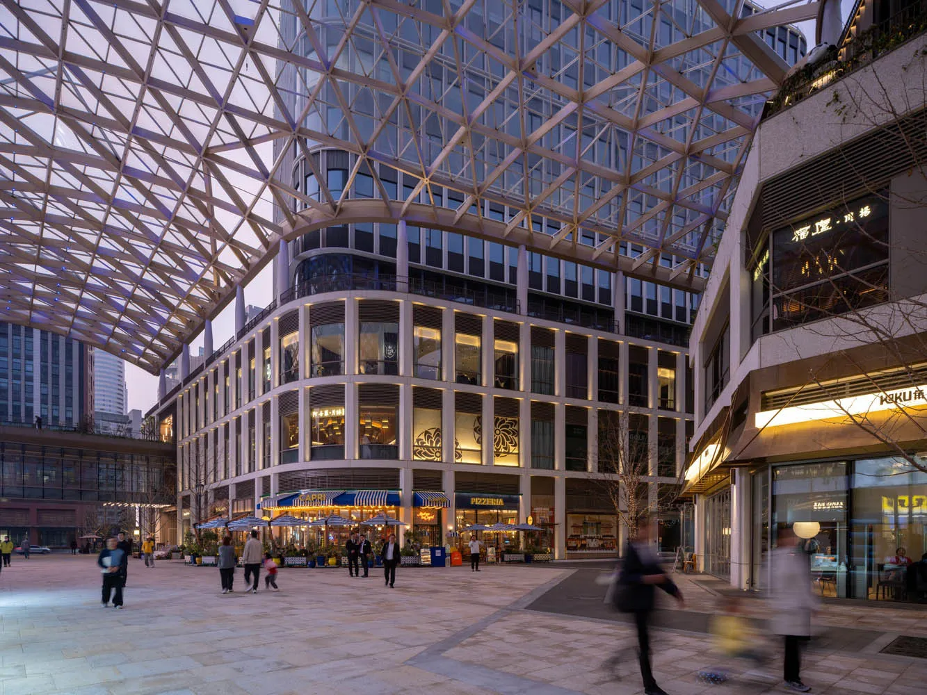 A bustling city street at night with a large building featuring a glass ceiling, surrounded by people and artificial lighting