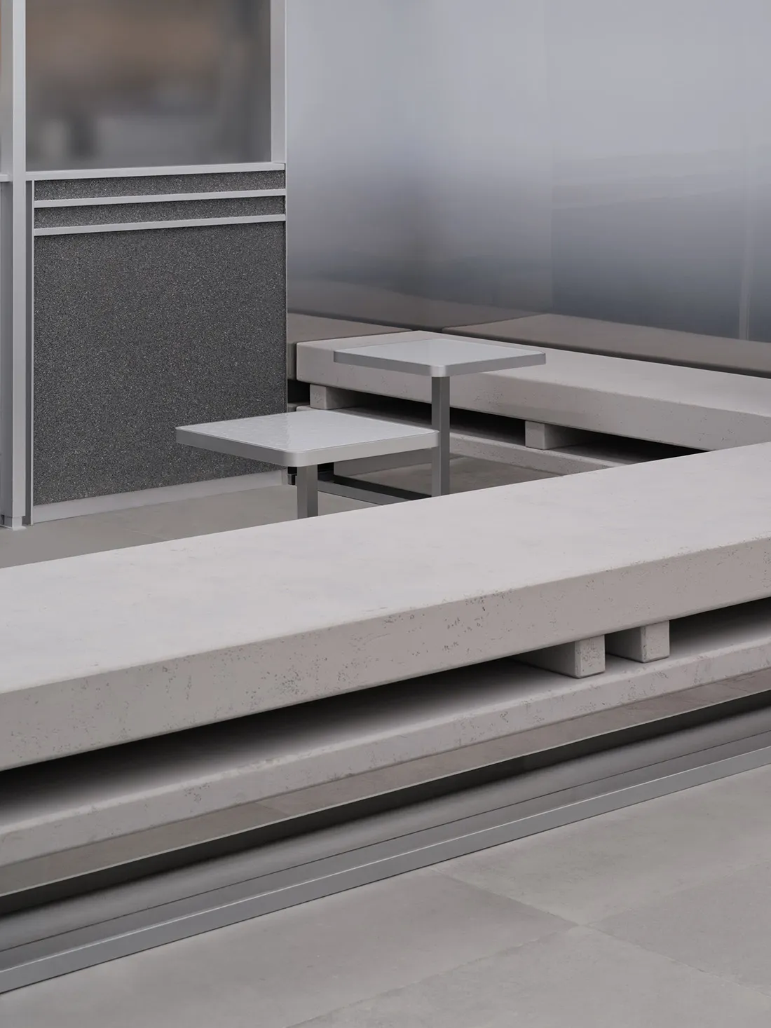 Dining area with a concrete bench and metal table in a well-lit room with a glass wall and cement floor
