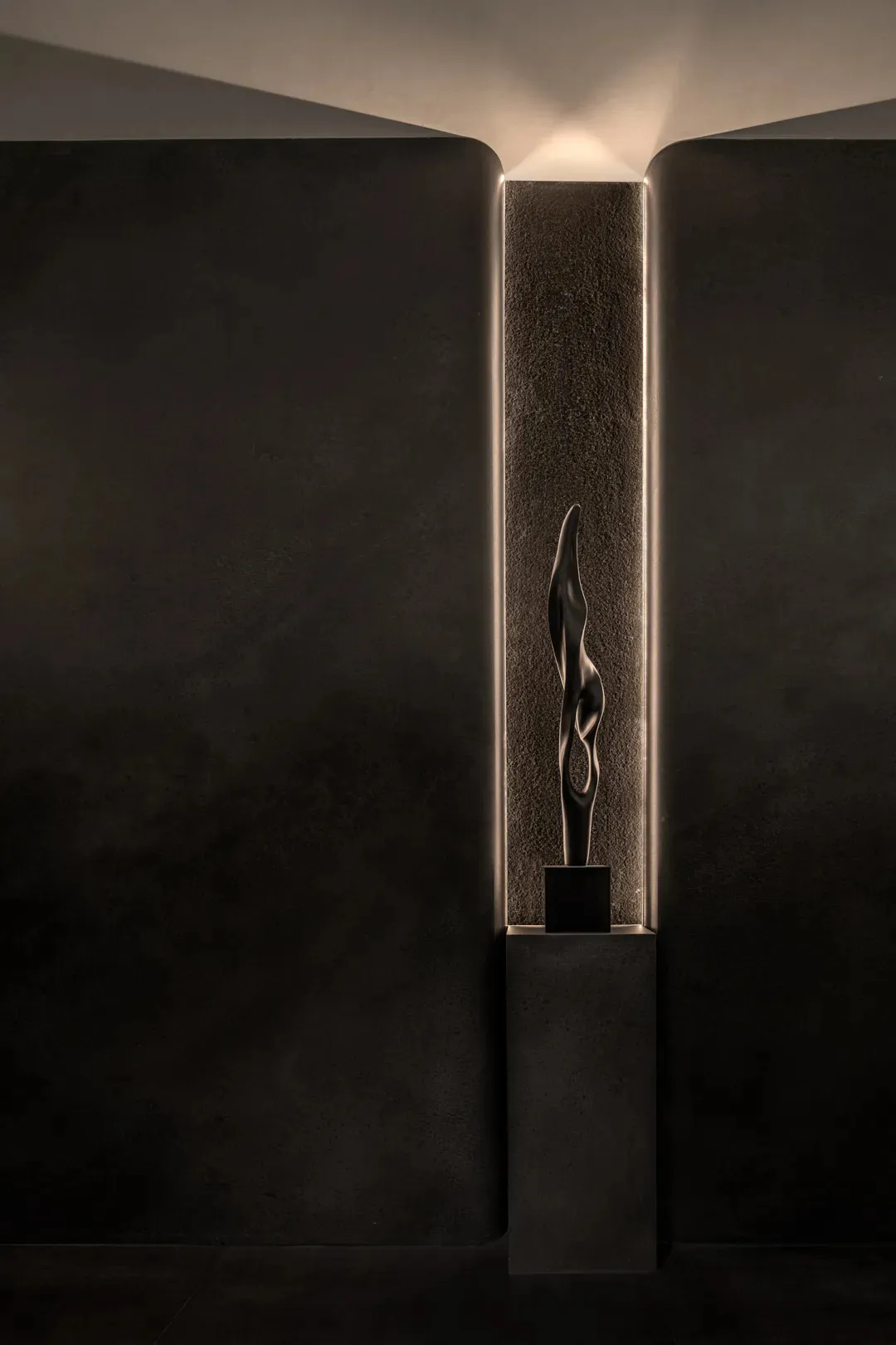 A black and white photograph of a modern metal sculpture on a pedestal in a dark room, with intricate details visible