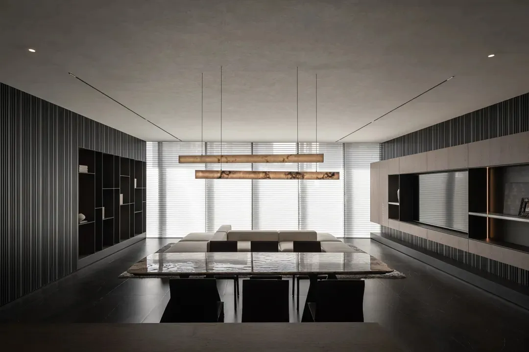 A spacious living room with a long dining table and chairs, a couch, and a hanging light fixture, in a contemporary style
