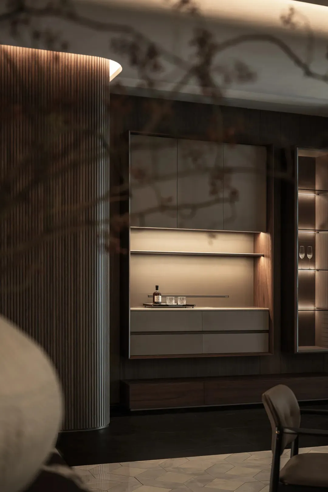 A modern kitchen with a wooden cabinet, glass door, and a countertop with a bottle and two cups
