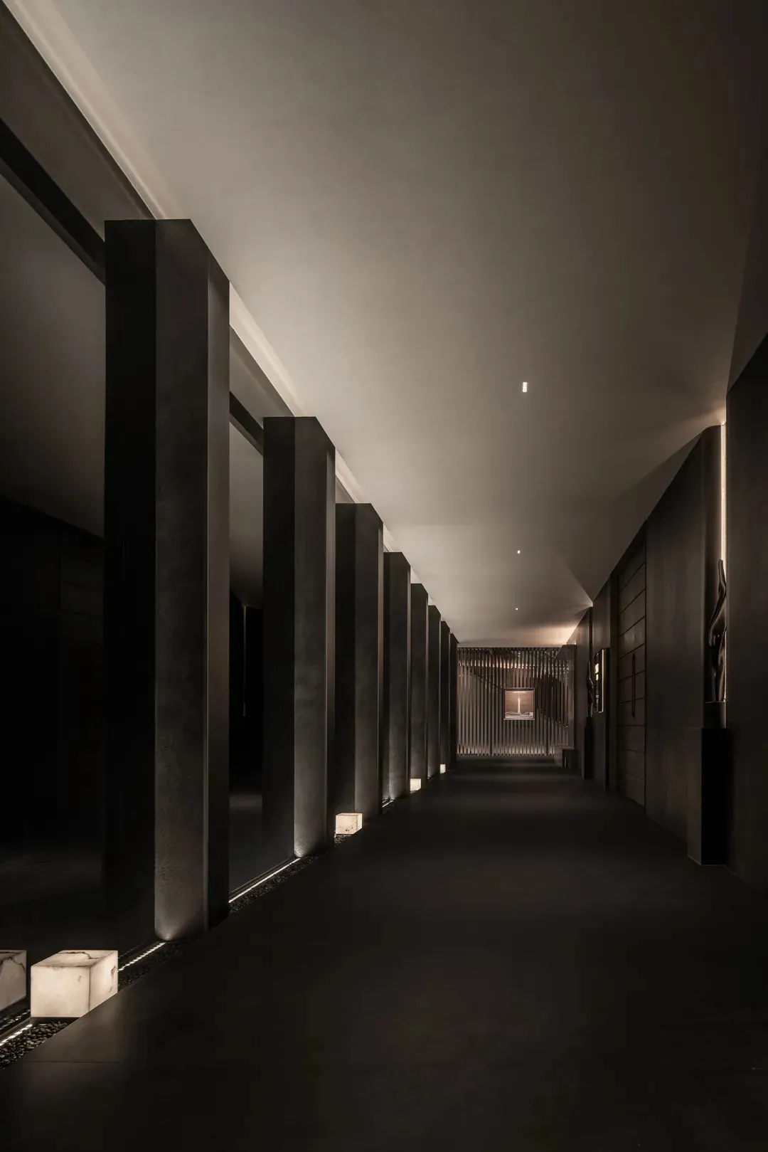 A dark and empty hallway with concrete pillars on either side, creating a sense of quietness and emptiness