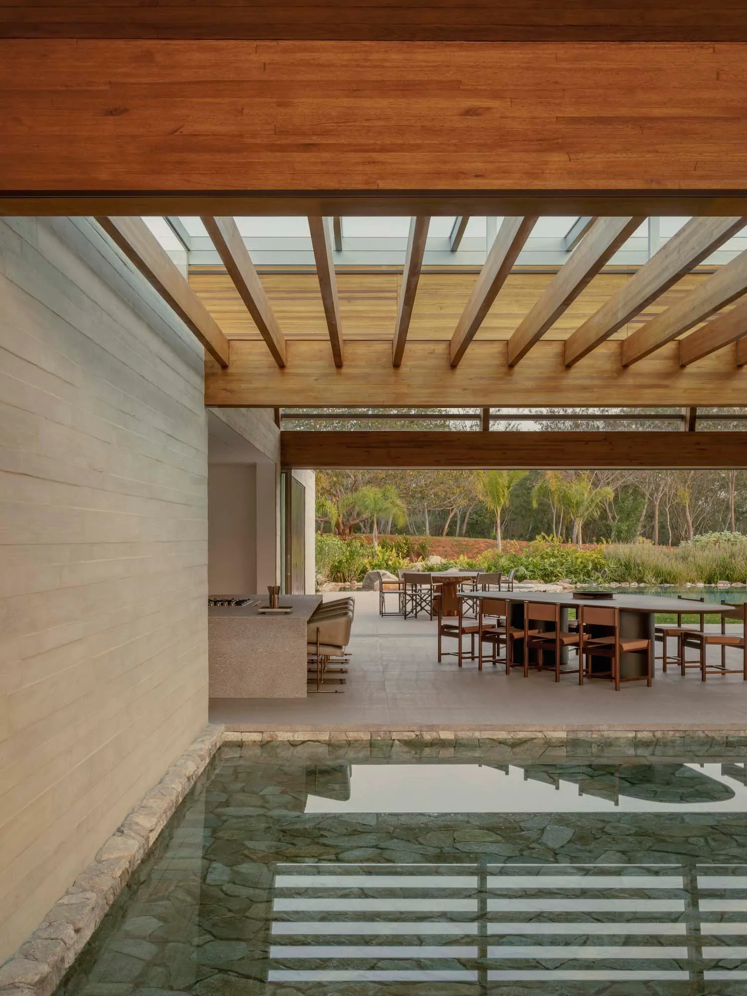 Large open living space with a pool and dining area, surrounded by furniture, wood, and stone, with natural light and a relaxed atmosphere