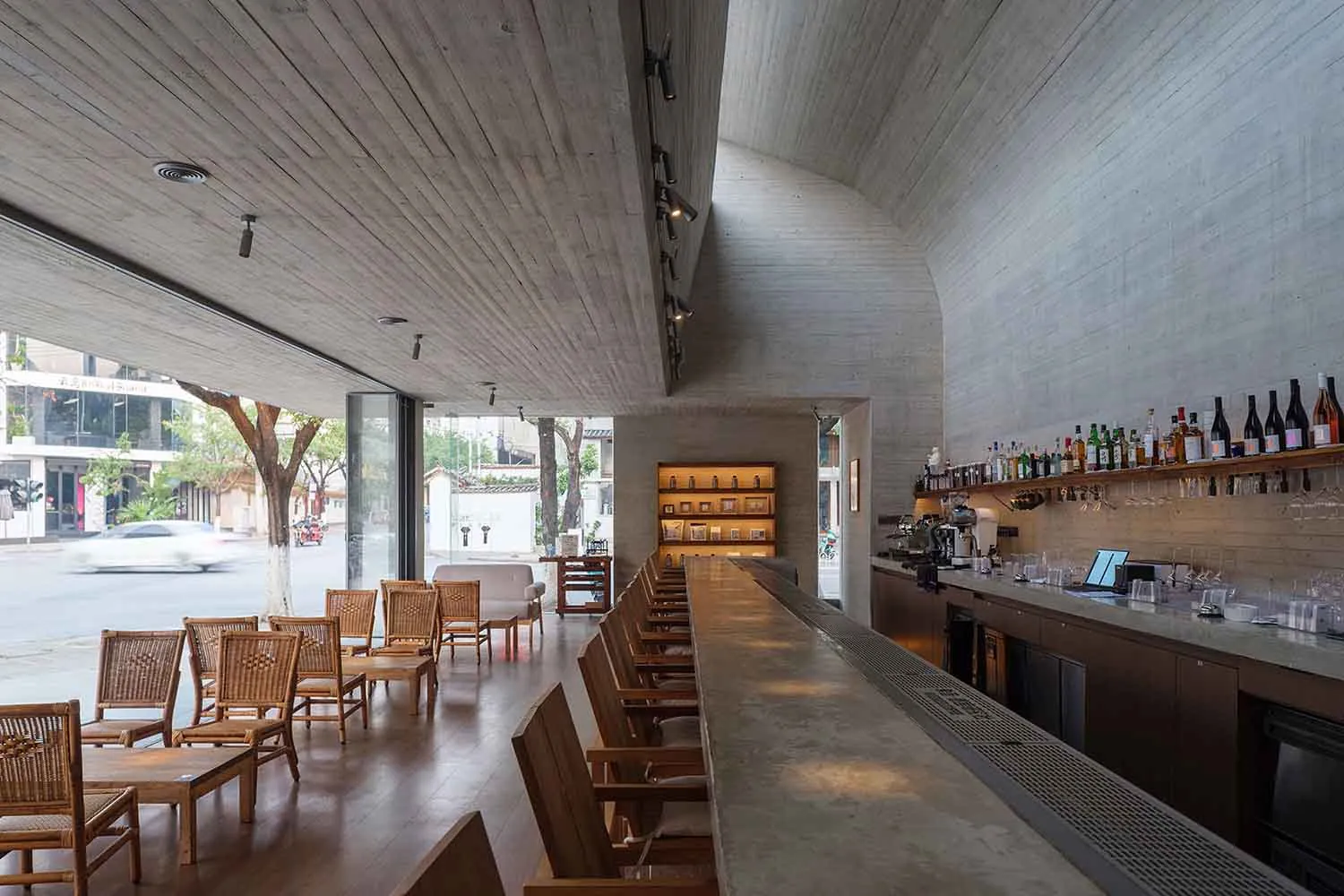 A warm and inviting bar with a wooden counter, table, and chairs, set against a wooden ceiling and floor, with bottles and cups on the counter