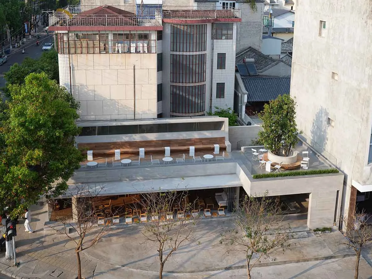 一座擁有大型玻璃牆與屋頂露台的現代建築，設有配備座椅和餐桌的戶外休憩區，搭配混凝土外牆，置於自然採光環境中