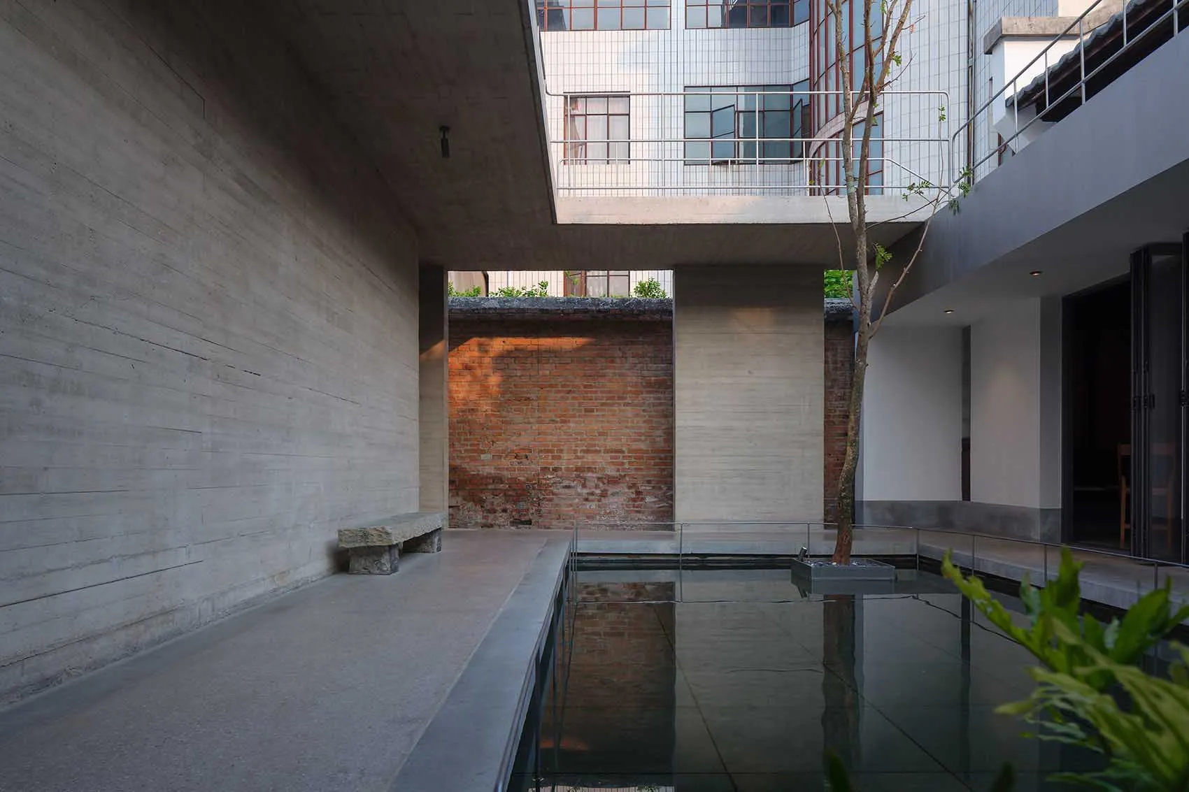 A bright and inviting open space with a large glass wall, a brick wall, and a pool of water, surrounded by a modern building with a focus on natural light