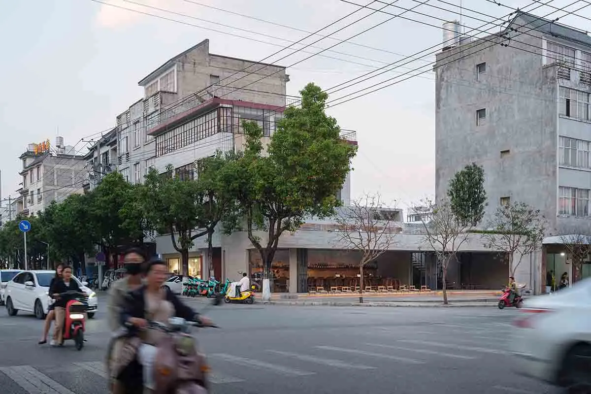 A busy city street with a tall building in the background, lined with trees and featuring motorcycles and pedestrians