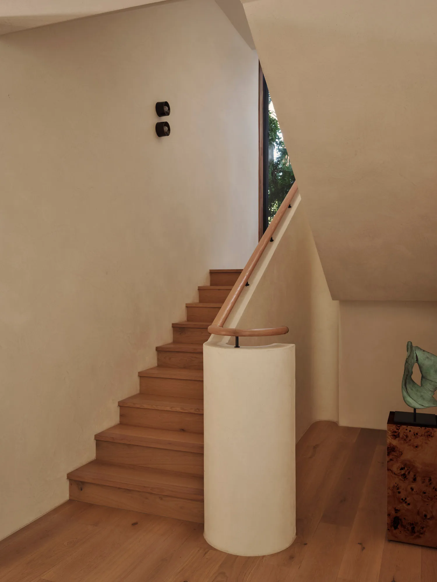 A wooden staircase with a white railing in a bright and welcoming hallway with a nearby window